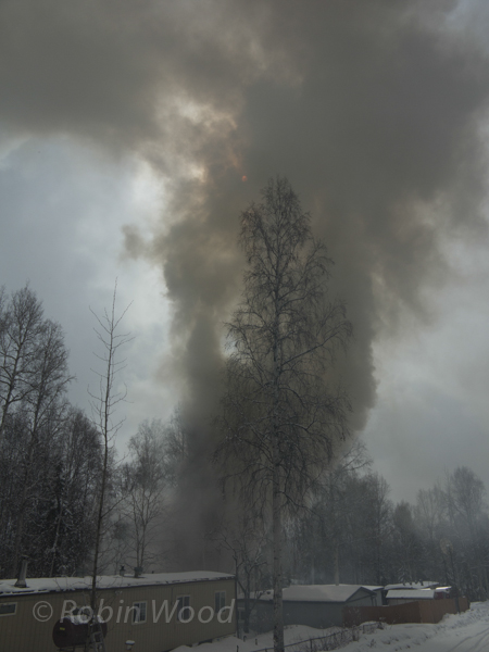 The sun is obscured by smoke rising from a fire in a residential neighborhood.