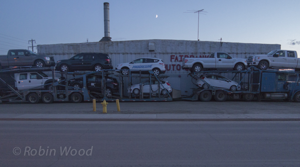 Car transport parked with crescent moon above. May 16, 12:02 a.m.