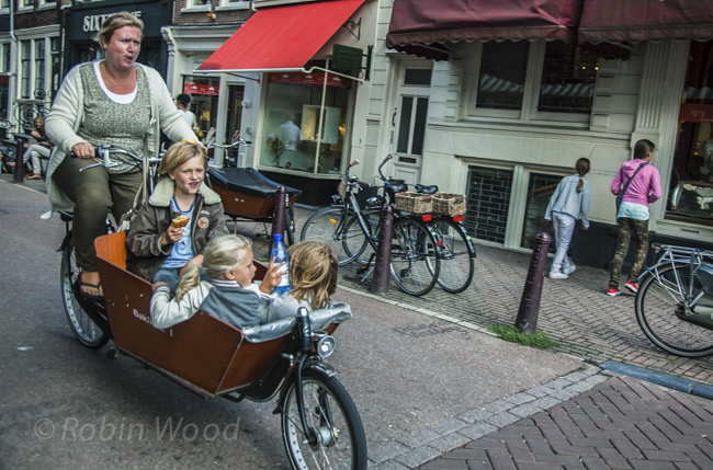 A determined mother shuttles children in a large basket on a bicycle. 